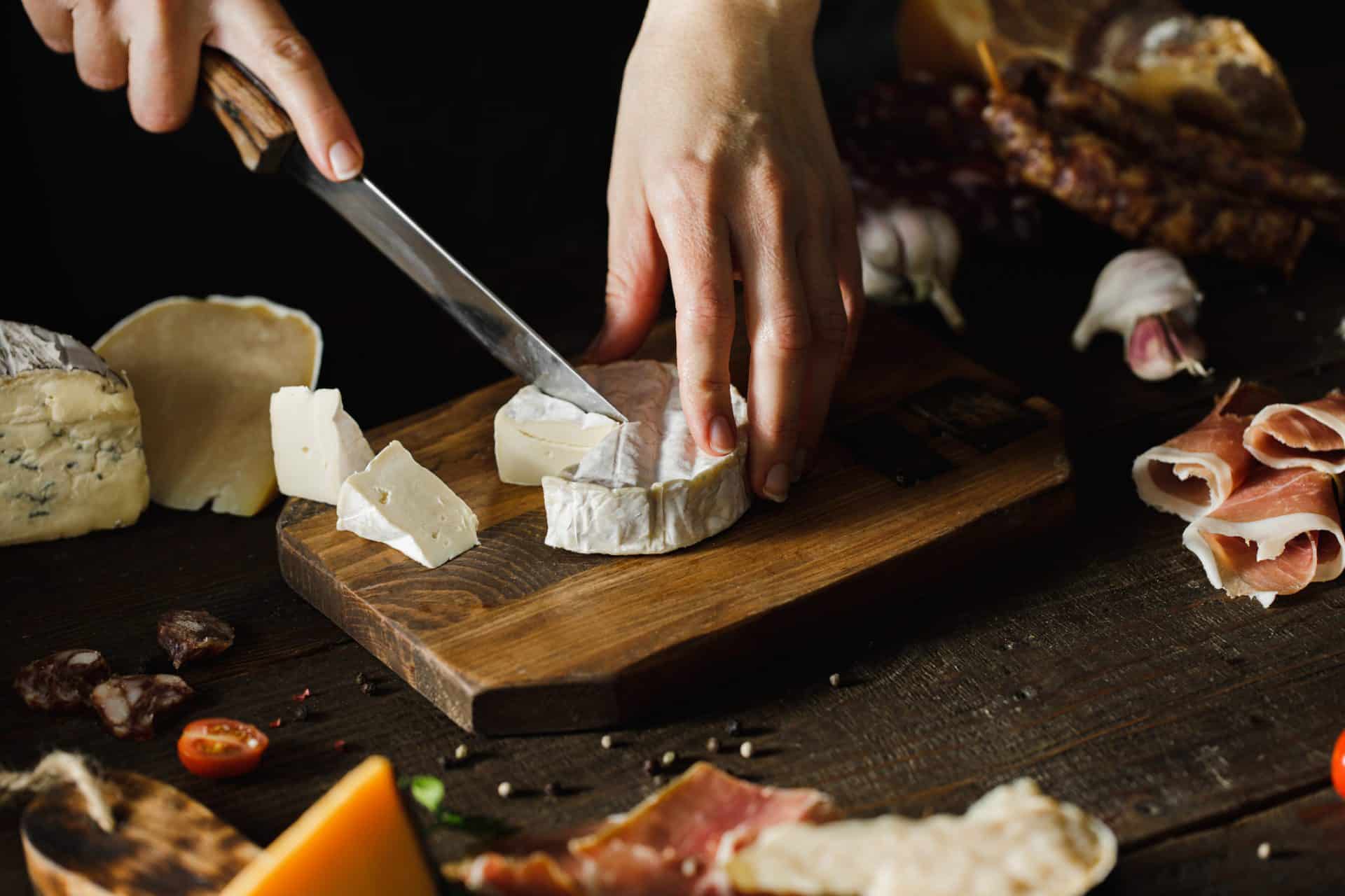 Woman hand cutting camembert on wooden board