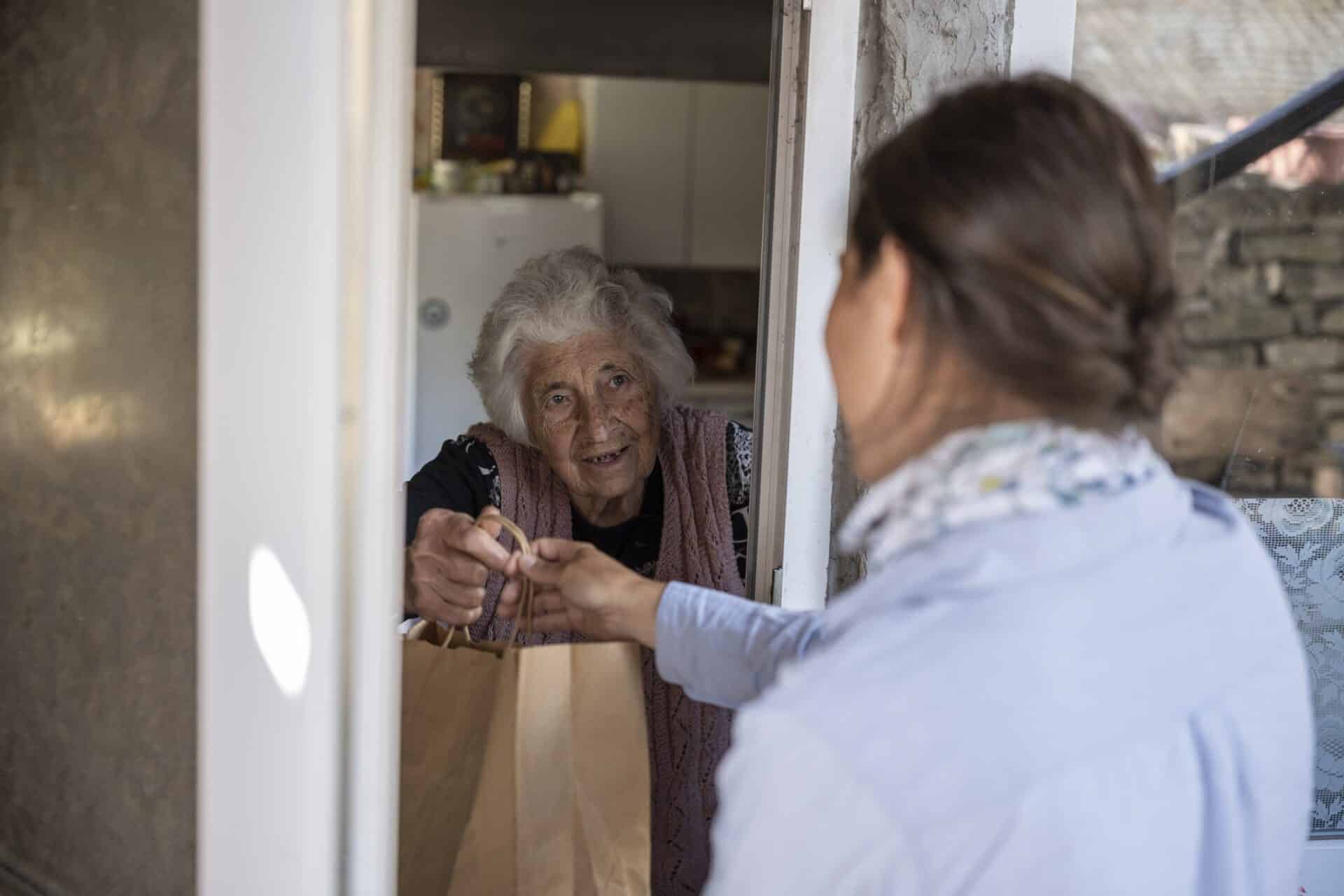 Volunteer delivering food to a senior woman at home.